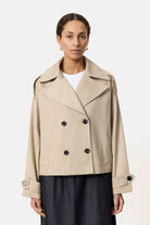 Beige Damen-Trenchcoat, kurz geschnitten, mit doppelreihigen Knöpfen und breitem Kragen. Modischer Mantel für Herbst und Frühling.