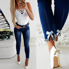 Damenmode: Elegante blaue Jeans mit Schleifen- und Perlendetails, kombiniert mit weißem Top und High Heels. Perfekt für stilvolle Outfits.