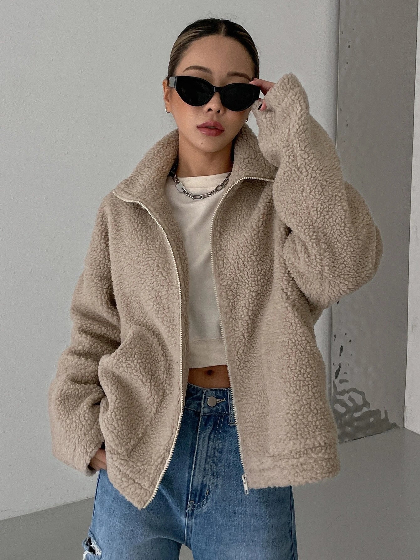 Damenmode: Trendige Teddyjacke in Beige, kombiniert mit lässiger Jeans und Sonnenbrille. Perfekt für stilvolle Herbst- und Winteroutfits.