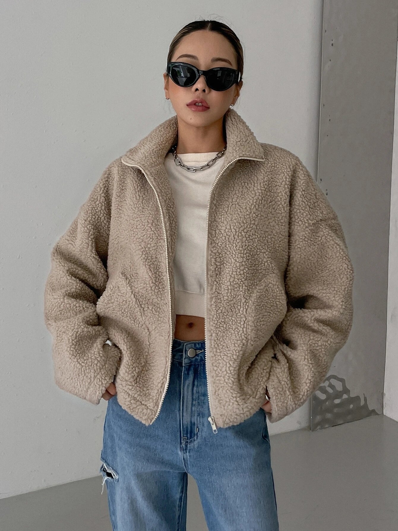 Flauschige Teddyjacke in Beige, kombiniert mit lässiger Jeans und Sonnenbrille. Perfekt für modische Herbst- und Winteroutfits.