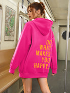 Frau in pinkem Oversize-Hoodie mit gelbem Schriftzug "Do What Makes You Happy" in U-Bahn. Modetrend, Streetwear, urbaner Stil, Hoodie.