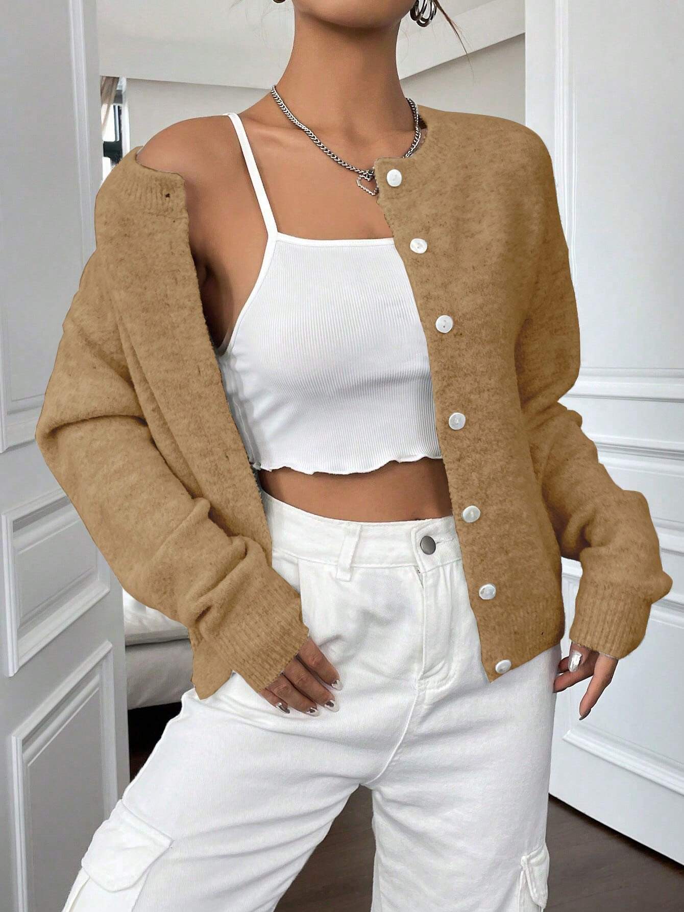 Damenmode: Beige Strickjacke über weißem Crop-Top, kombiniert mit weißen High-Waist-Hosen. Trendige Herbstmode, lässig und stilvoll.