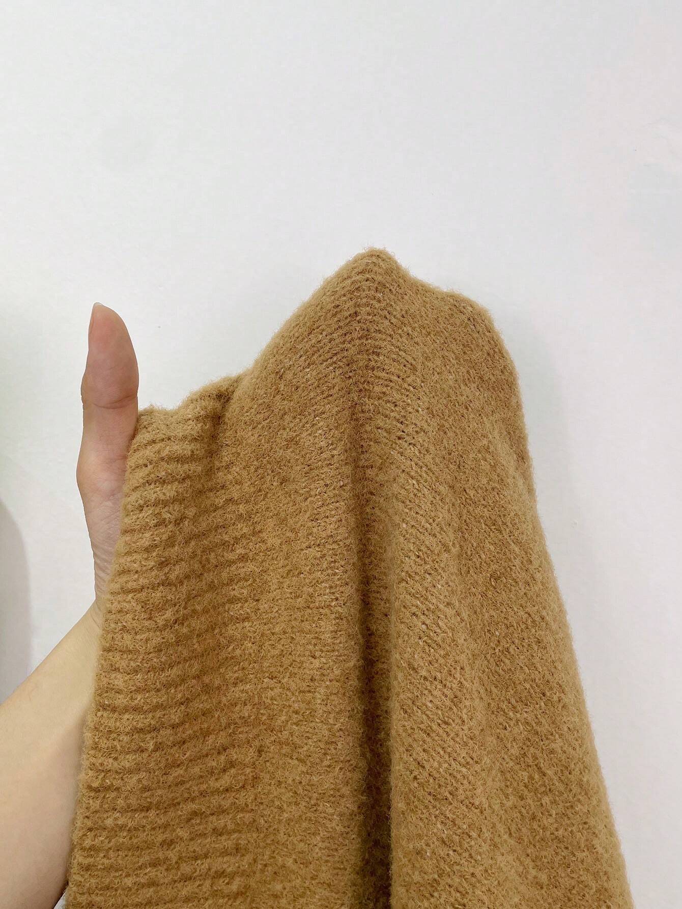 Kamelhaarstoff in Hand gehalten, weiche Textur, beige Farbe, ideal für hochwertige Bekleidung, luxuriöses Material, nachhaltige Mode.