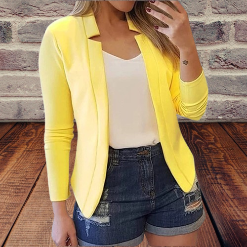 Gelber Blazer Damen, kombiniert mit weißem Top und Jeansshorts, vor Backsteinwand. Modetrend, lässiger Look, Frühlingsoutfit, Streetstyle.