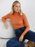 Frau in orangefarbenem Rollkragenpullover und blauer Jeans, lässig sitzend. Modetrend, Herbstmode, Damenbekleidung, stilvoll, bequem.