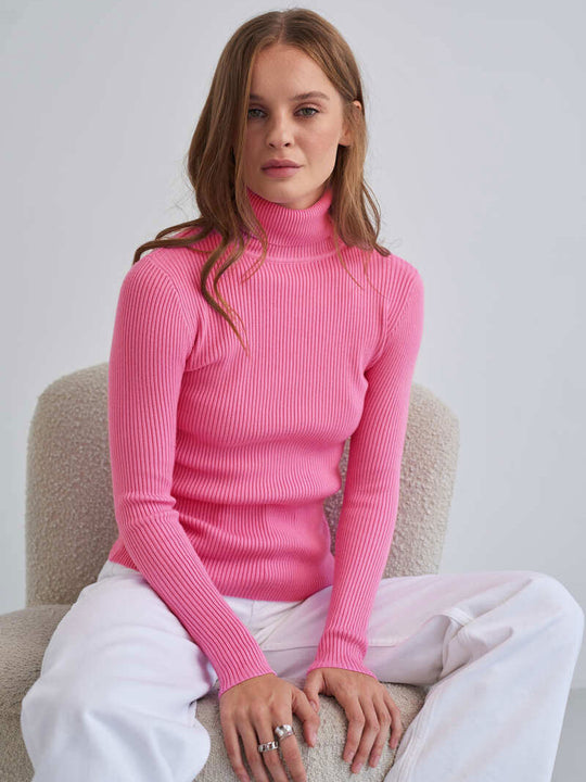 Frau in rosa Rollkragenpullover, sitzt entspannt. Modetrend, Damenmode, Strickpullover, Herbstmode, stilvoll, bequem, modern.