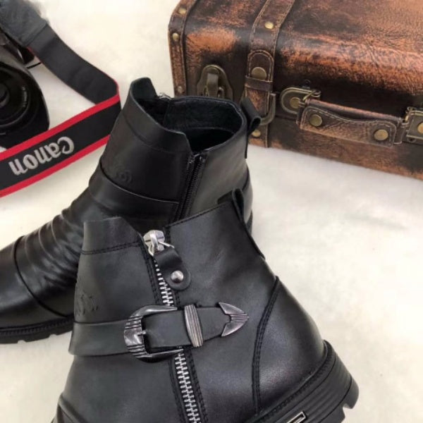 Schwarze Lederstiefel mit Reißverschluss und Schnalle, neben einer Vintage-Ledertasche und einer Canon-Kamera. Hochwertige Herrenschuhe.