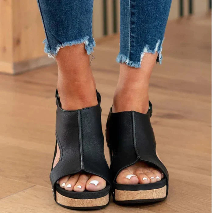 Schwarze Sandaletten mit Keilabsatz, offener Zehenpartie und Korksohle, kombiniert mit zerrissenen Jeans. Perfekt für Sommermode und Freizeitlook.