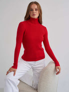 Frau in rotem Rollkragenpullover und weißer Hose, sitzt auf modernem Stuhl. Modetrend, stilvolle Damenbekleidung, elegantes Design.