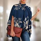 Elegante Frau in blauem, floralem Poncho mit brauner Lederhandtasche. Modetrend, Damenmode, stilvolle Kleidung, Accessoires, Herbstoutfit.