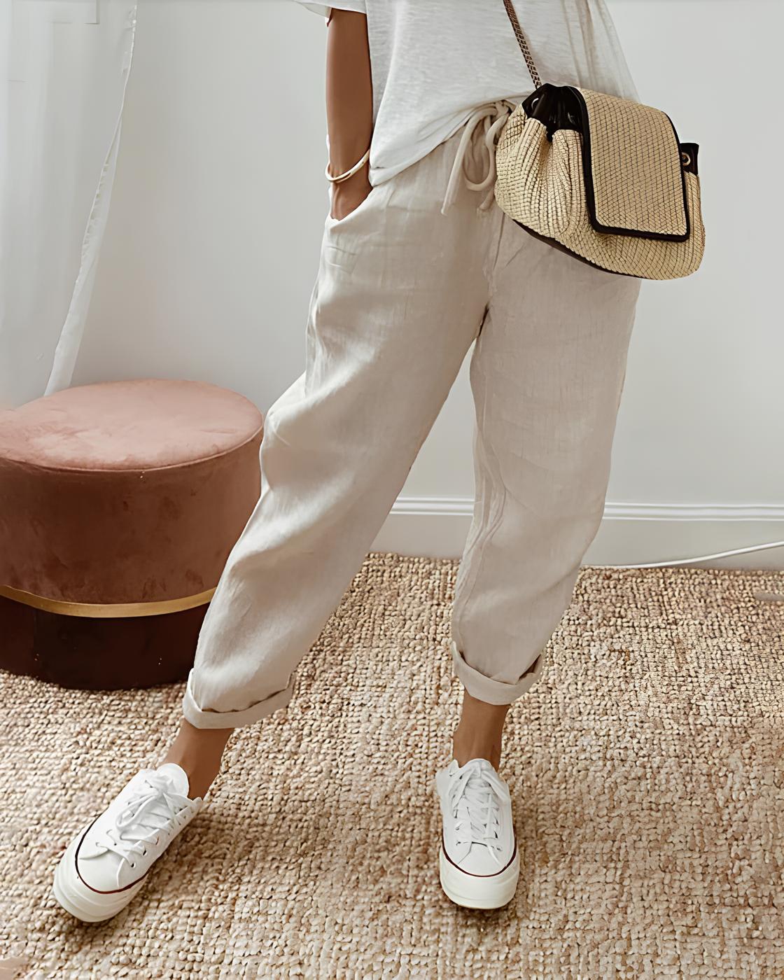 Beige Leinenhose Damen, lässig und bequem, kombiniert mit weißen Sneakers und Strohtasche. Perfekt für Sommermode und Freizeitoutfits.