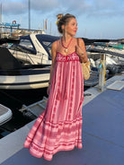 Frau in langem, rotem Boho-Kleid mit Spaghettiträgern am Hafen. Sommermode, Bohemian-Stil, Maxikleid, maritimes Ambiente.