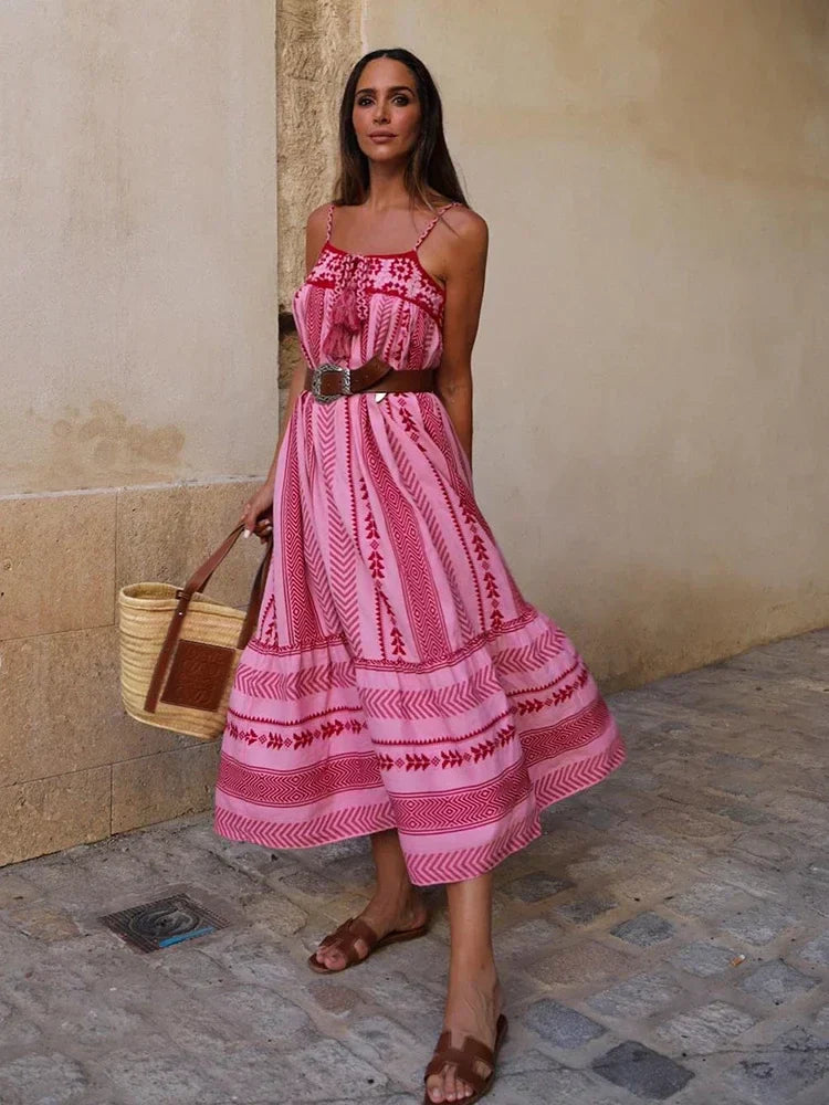 Frau in einem langen, rosa Boho-Kleid mit Spaghettiträgern und Gürtel, trägt eine Strohtasche. Sommermode, Bohemian-Stil, Damenbekleidung.