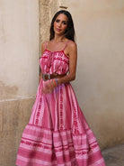 Frau in langem, rosa Boho-Kleid mit Spaghettiträgern und Ethno-Muster. Perfekt für Sommermode, Strandkleid, femininer Look.