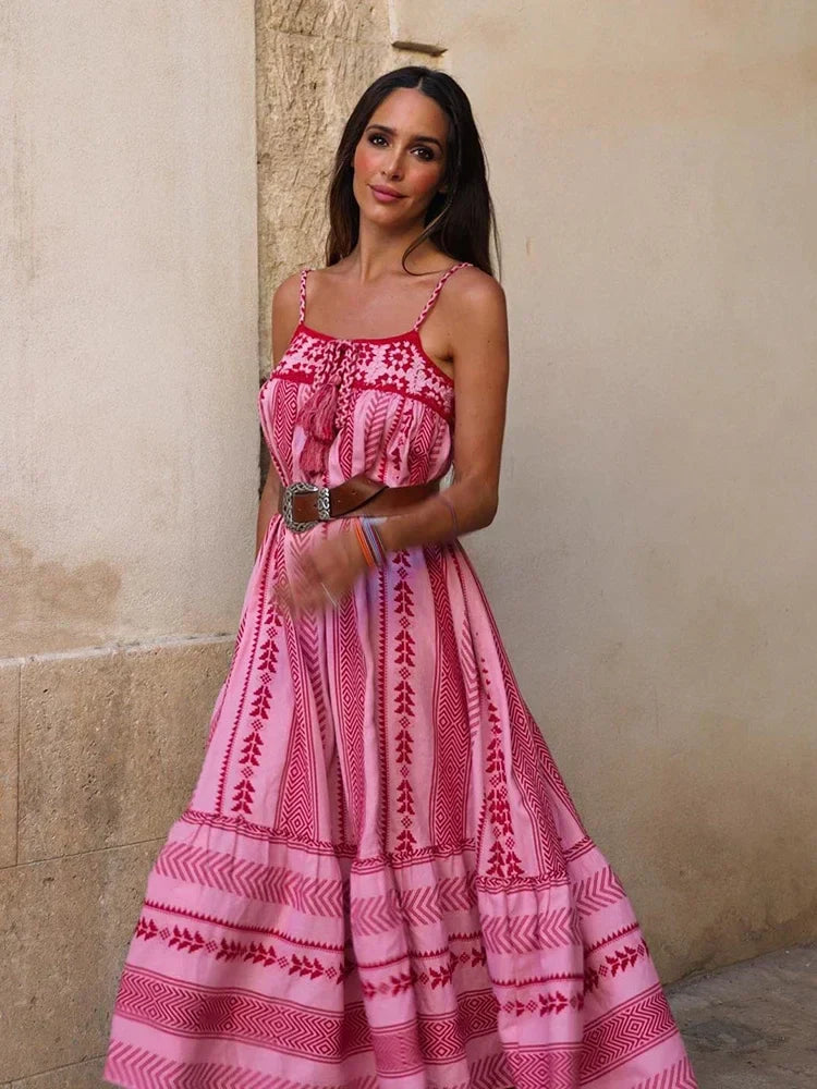 Frau in langem, rosa Boho-Kleid mit Spaghettiträgern und Ethno-Muster. Perfekt für Sommermode, Strandkleid, femininer Look.