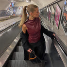 Frau in eleganter, ärmelloser Lederbluse auf Rolltreppe in U-Bahn-Station. Mode, urbane Eleganz, stilvolle Kleidung, Accessoires.