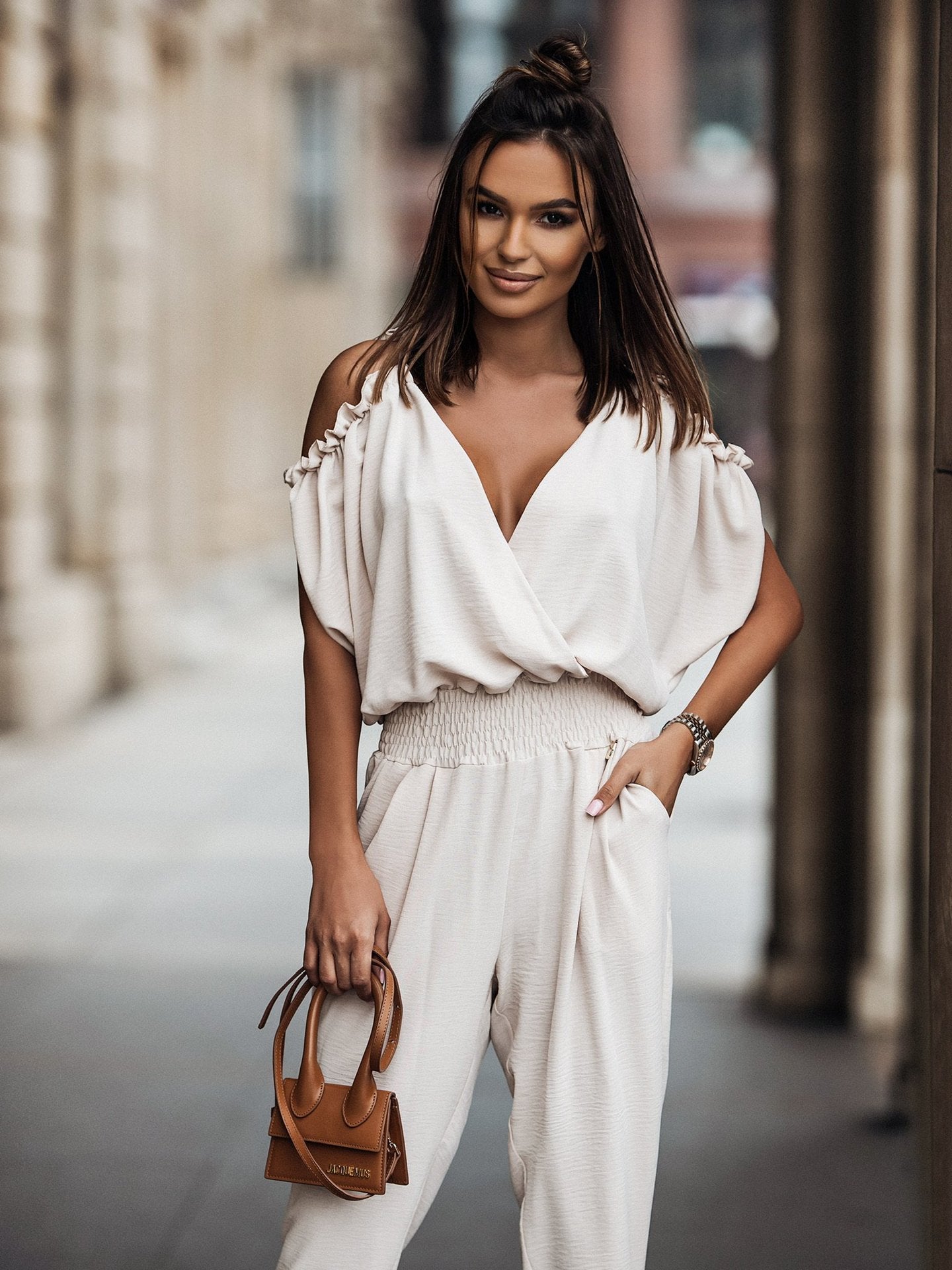 Frau in stilvollem, cremefarbenem Jumpsuit mit modischer Handtasche. Perfektes Outfit für urbane Eleganz und trendige Streetwear.