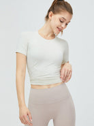 Damen-Sportoutfit: Weißes, kurzärmeliges Crop-Top und beige Leggings. Perfekt für Fitness, Yoga und Freizeit. Bequem und stilvoll.