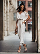 Elegantes Damen-Outfit: Weißer Jumpsuit mit V-Ausschnitt, kombiniert mit Sandalen und brauner Handtasche. Perfekt für den Sommer-Look.