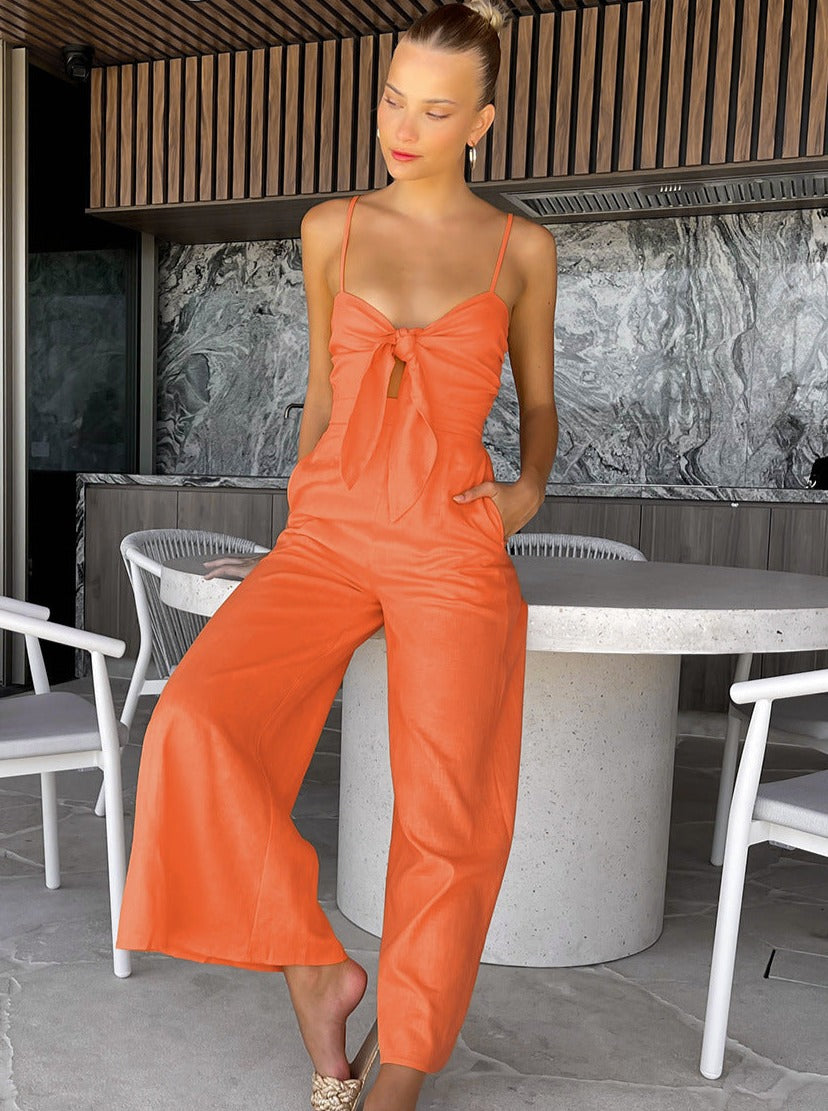 Frau in orangefarbenem Jumpsuit vor modernem Interieur. Sommermode, eleganter Look, trendige Damenbekleidung, stilvolle Outfits.