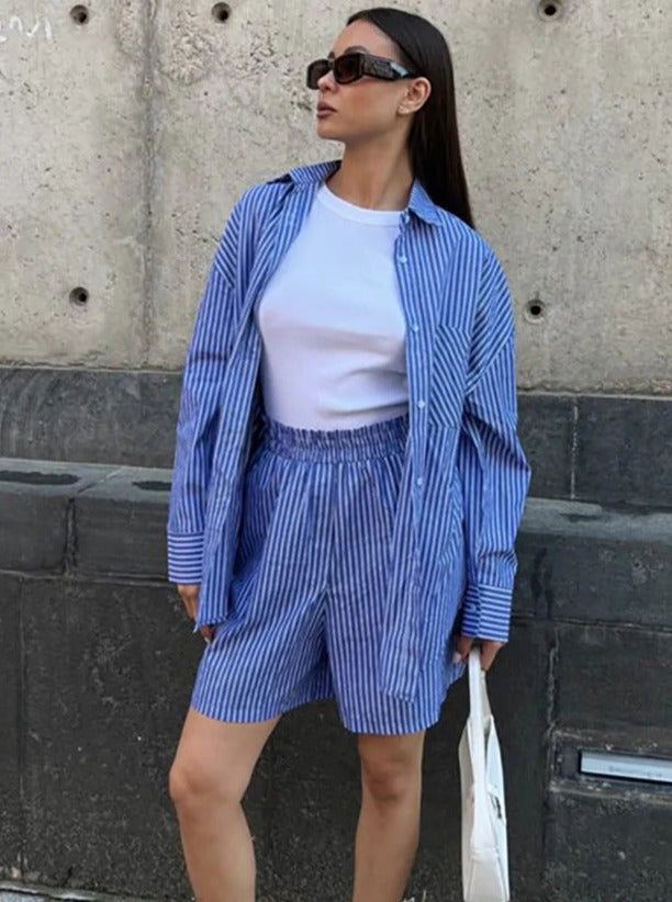 Frau in gestreiftem blau-weißem Hemd und Shorts, trägt Sonnenbrille und weiße Tasche. Modetrend, Sommeroutfit, lässiger Stil.