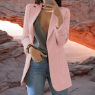 Frau in rosa Blazer vor Felsbogen, modisch gekleidet, Jeans, graues Top. Stilvolle Damenmode, Outdoor-Hintergrund, trendige Outfits.