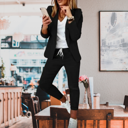 Elegante Frau im schwarzen Blazer und Jogginghose, hält Smartphone. Modetrend, Business-Casual, stilvolle Damenbekleidung, urbaner Look.