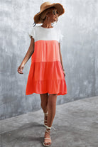 Frau im Sommerkleid in Orange und Weiß, Strohhut, Sandalen. Perfekt für Strandmode, lässiger Sommerlook, Damenbekleidung.