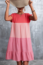 Frau in einem farbenfrohen, gestuften Sommerkleid in Rosa- und Rottönen, hält einen Strohhut. Modetrend, Sommermode, Damenkleid, Freizeitlook.