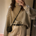 Gestreifter Rollkragenpullover in Beige und Schwarz, kombiniert mit beigen Hosen und schwarzer Umhängetasche. Modischer Herbst-Look für Damen.