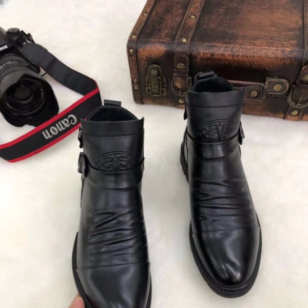 Schwarze Lederstiefel mit Schnallen, elegant und stilvoll, neben einer Vintage-Ledertasche und einer Canon-Kamera auf weißem Hintergrund.