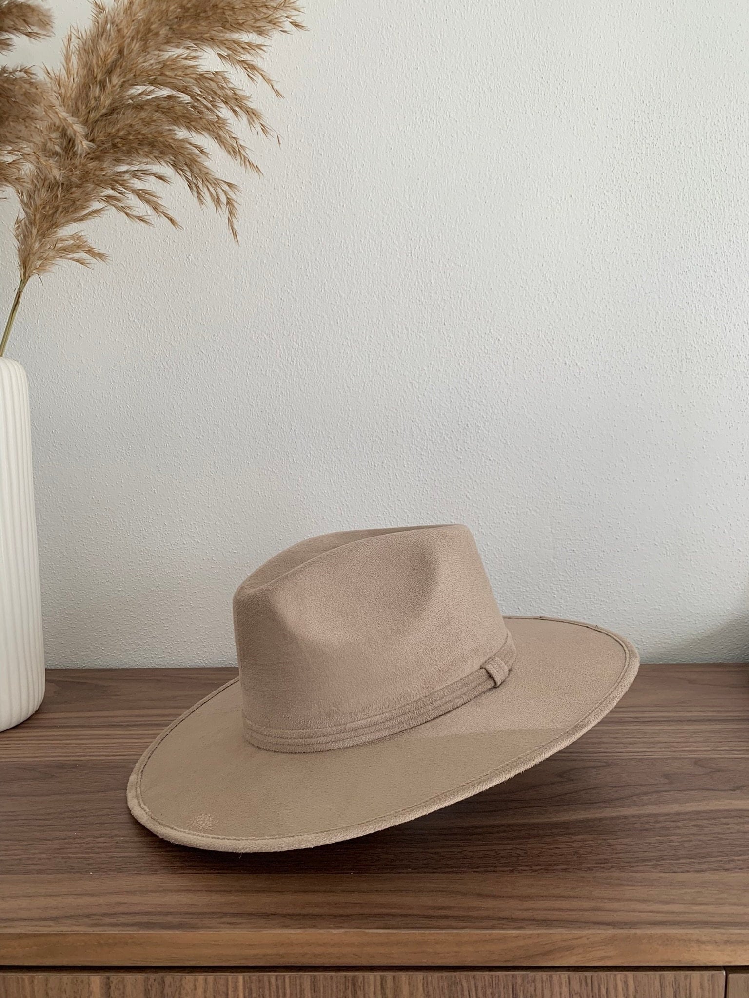 Beiger Fedora-Hut aus Filz auf Holztisch, minimalistisch dekoriert mit Pampasgras in Vase. Perfekt für stilvolle Mode und Accessoires.