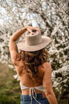 Frau mit Hut vor blühenden Kirschblüten, Rückenansicht. Frühling, Natur, Mode, Outdoor, Jeans, Strohhut, Blumen, romantische Atmosphäre.