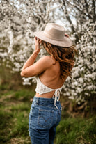 Frau in Jeans und Häkeloberteil vor blühenden Bäumen, trägt Hut. Frühling, Mode, Natur, Outdoor-Fotografie, lässiger Stil.