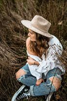 Frau in zerrissenen Jeans und weißem Hemd, sitzt im Gras, trägt einen beigen Hut. Mode, Outdoor, lässiger Stil, Herbstlook, Natur.