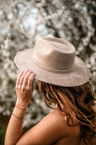 Frau mit beigem Filzhut vor blühendem Baum. Modetrend, stilvoller Damenhut, Frühlingsmode, Accessoires, Naturhintergrund, eleganter Look.