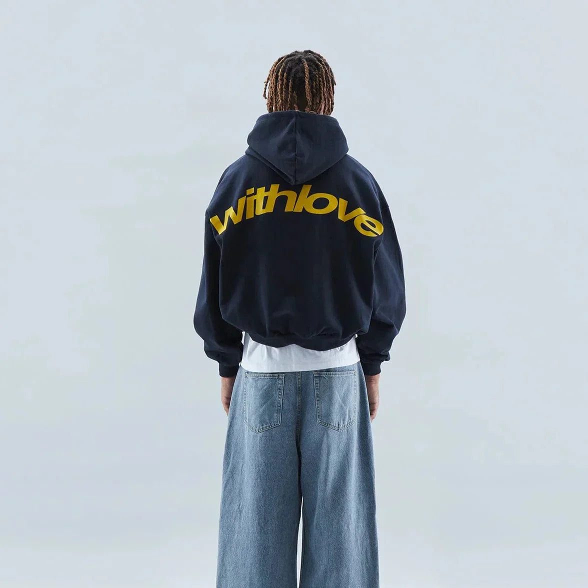 Schwarzer Hoodie mit gelbem "withlove"-Schriftzug, getragen von Person mit blauen Jeans. Modetrend, Streetwear, lässiger Stil.